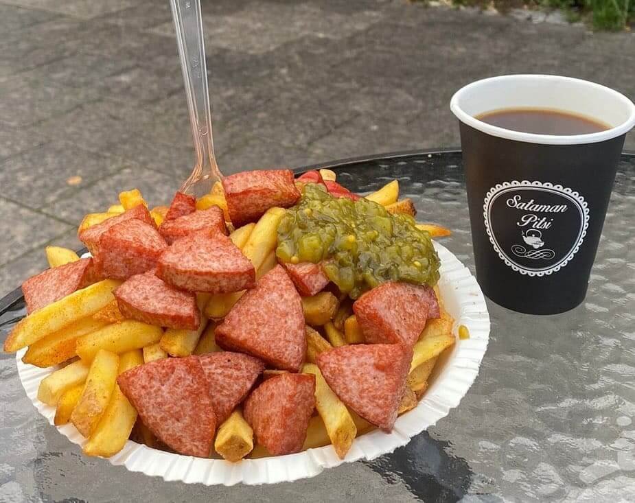 Lappeenrannan Sataman Pitsin herkulliset makkaraperunat ranskalaisilla sekä suolakurkuilla. Grilliherkun vieressä on kuppi maistuvaa kahvia. Kuva otettu Lappeenrannan Satamatorilla, jossa Sataman Pitsi myös sijaitsee.